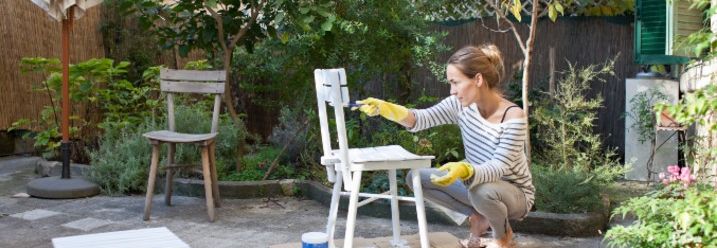 Frau lackiert Stuhl in Garten